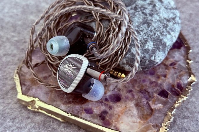  Kiwi Ears Aether planar-magnetic IEMs sitting on a rock on top of a purple and gold coaster