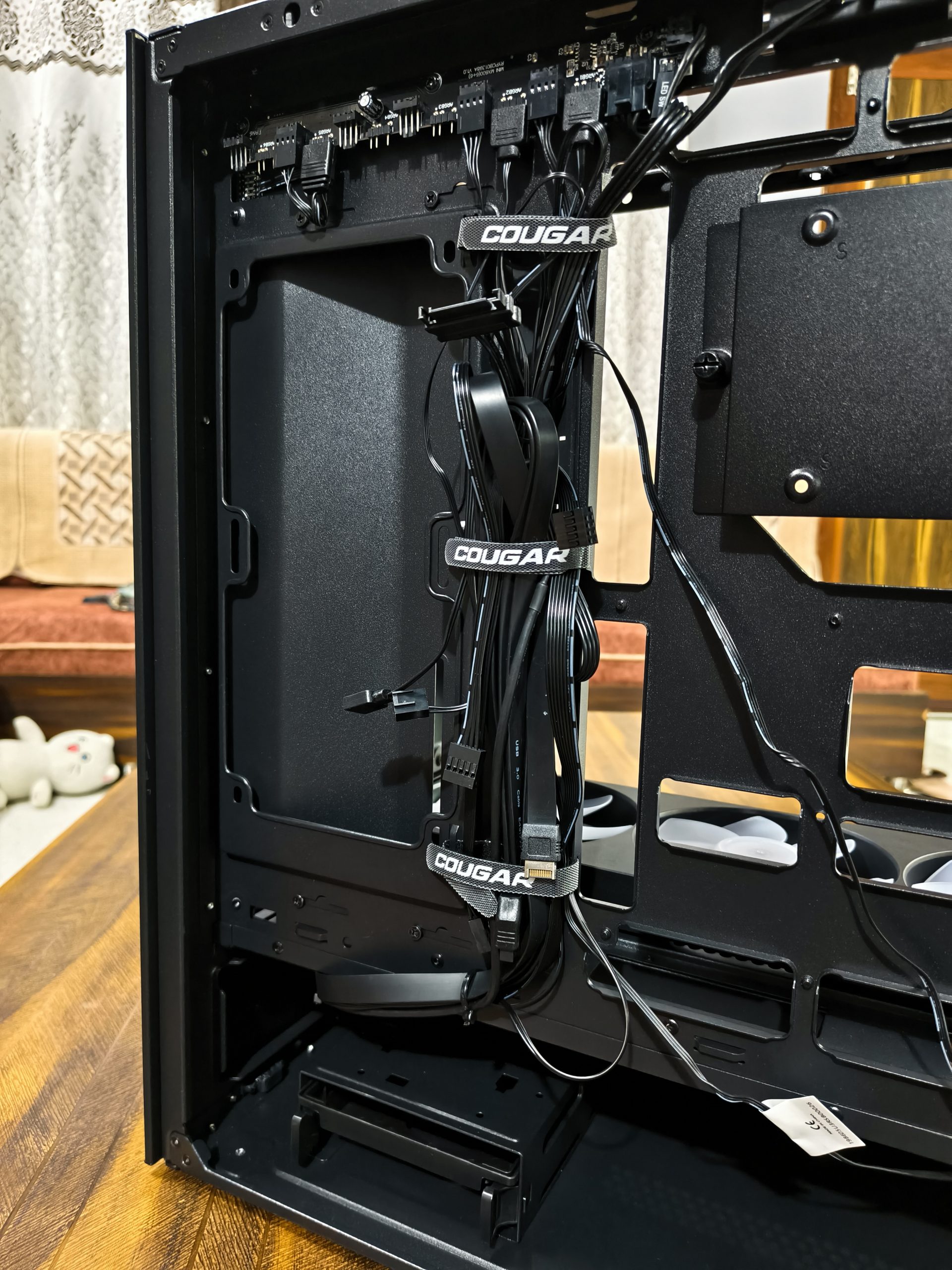 Το εσωτερικό μιας θήκης υπολογιστή μεσαίου πύργου που δείχνει τη διαχείριση καλωδίων δεμένη με ιμάντες επωνυμίας «COUGAR».