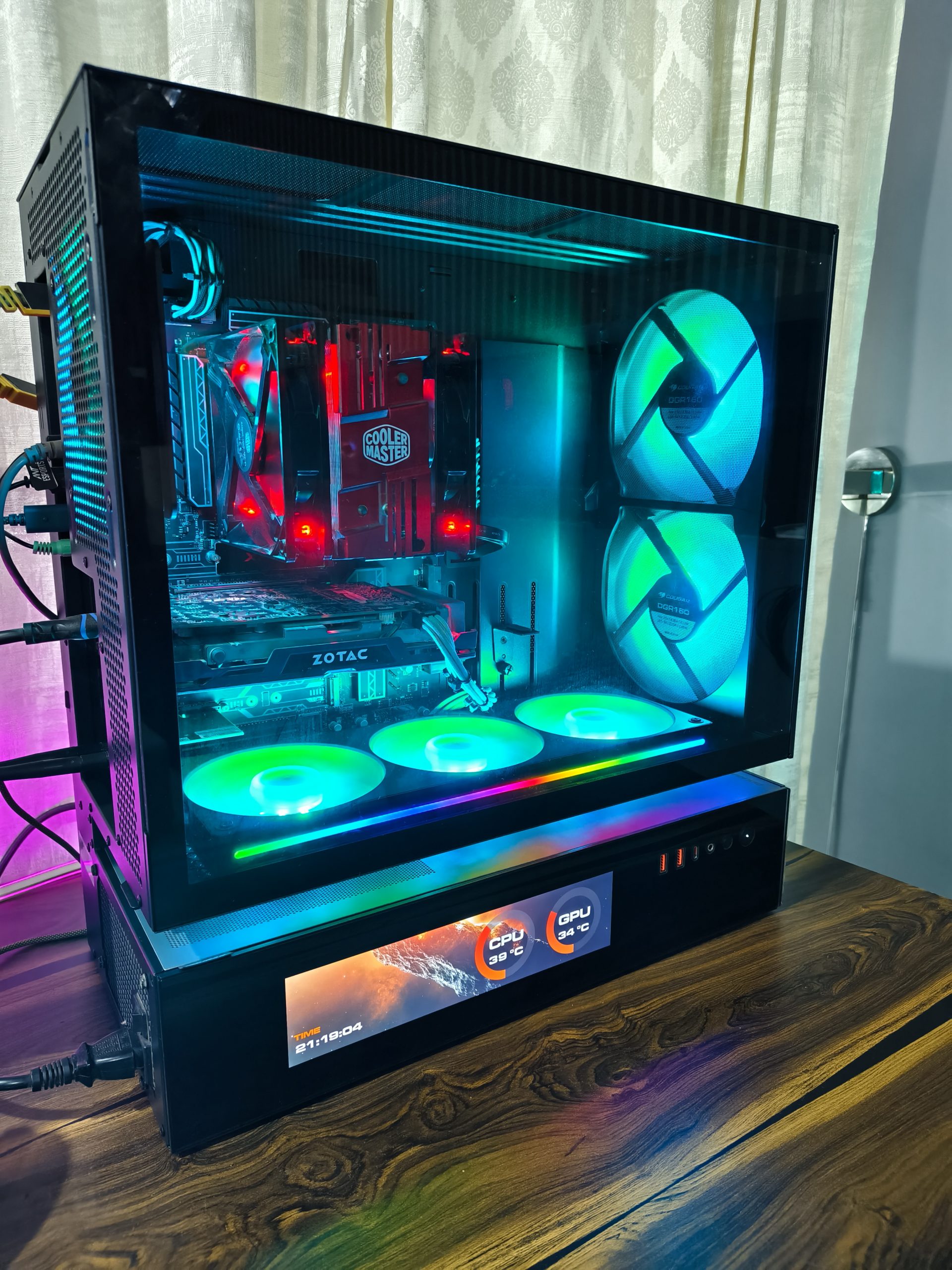 Ένας υπολογιστής παιχνιδιών με εξαρτήματα Cooler Master, κάρτα γραφικών Zotac, ανεμιστήρες ψύξης RGB και οθόνη που δείχνει «CPU 39°C» και «GPU 34°C».