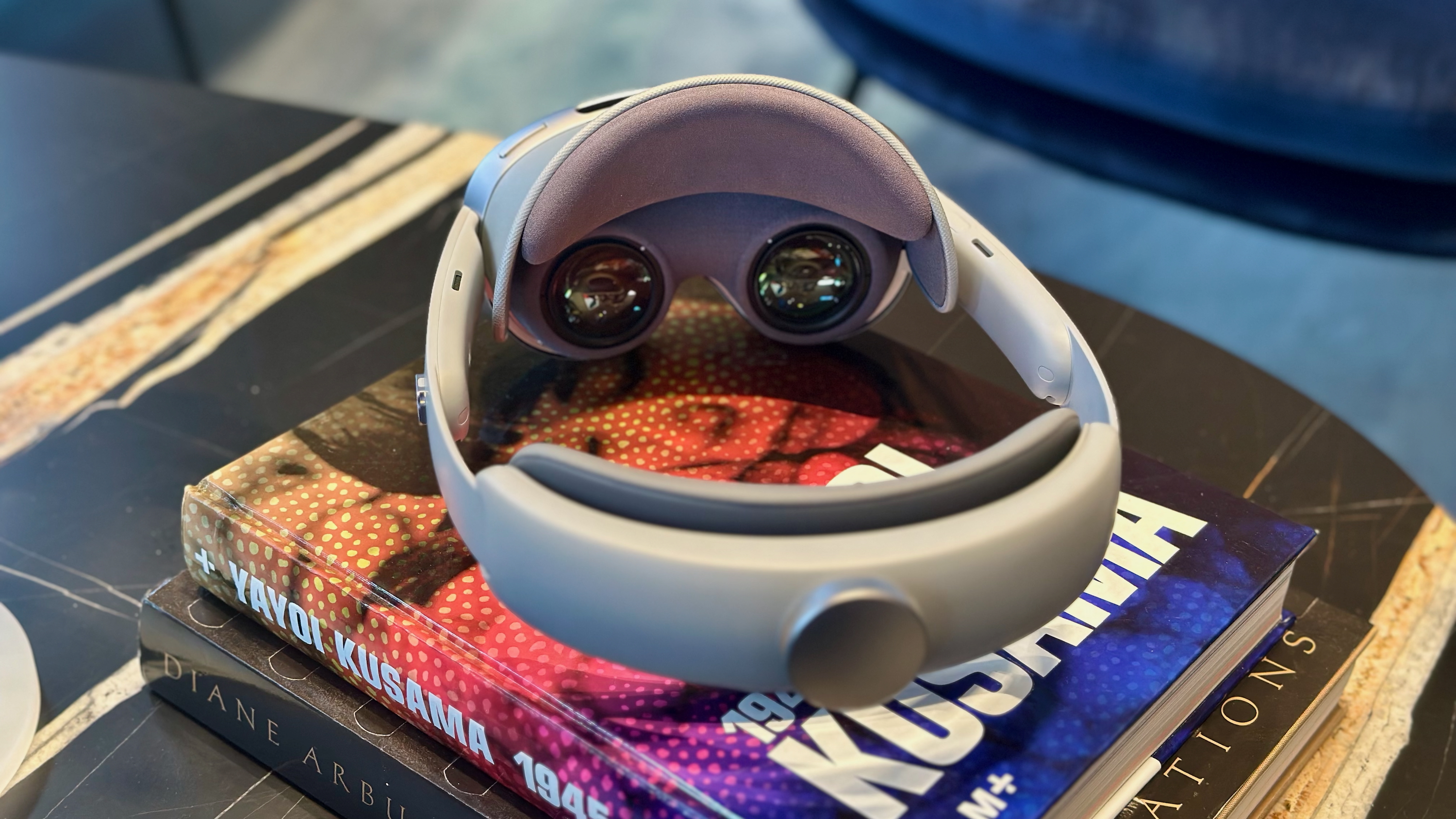 A photo of the Samsung Galaxy XR headset sitting on a pile of books, angled away to show the lenses and back knob. 