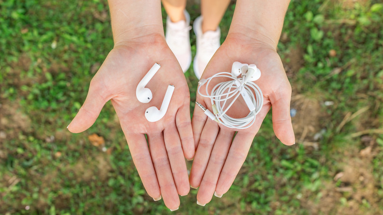 Χέρια που κρατούν ασύρματα και ενσύρματα ακουστικά δίπλα-δίπλα