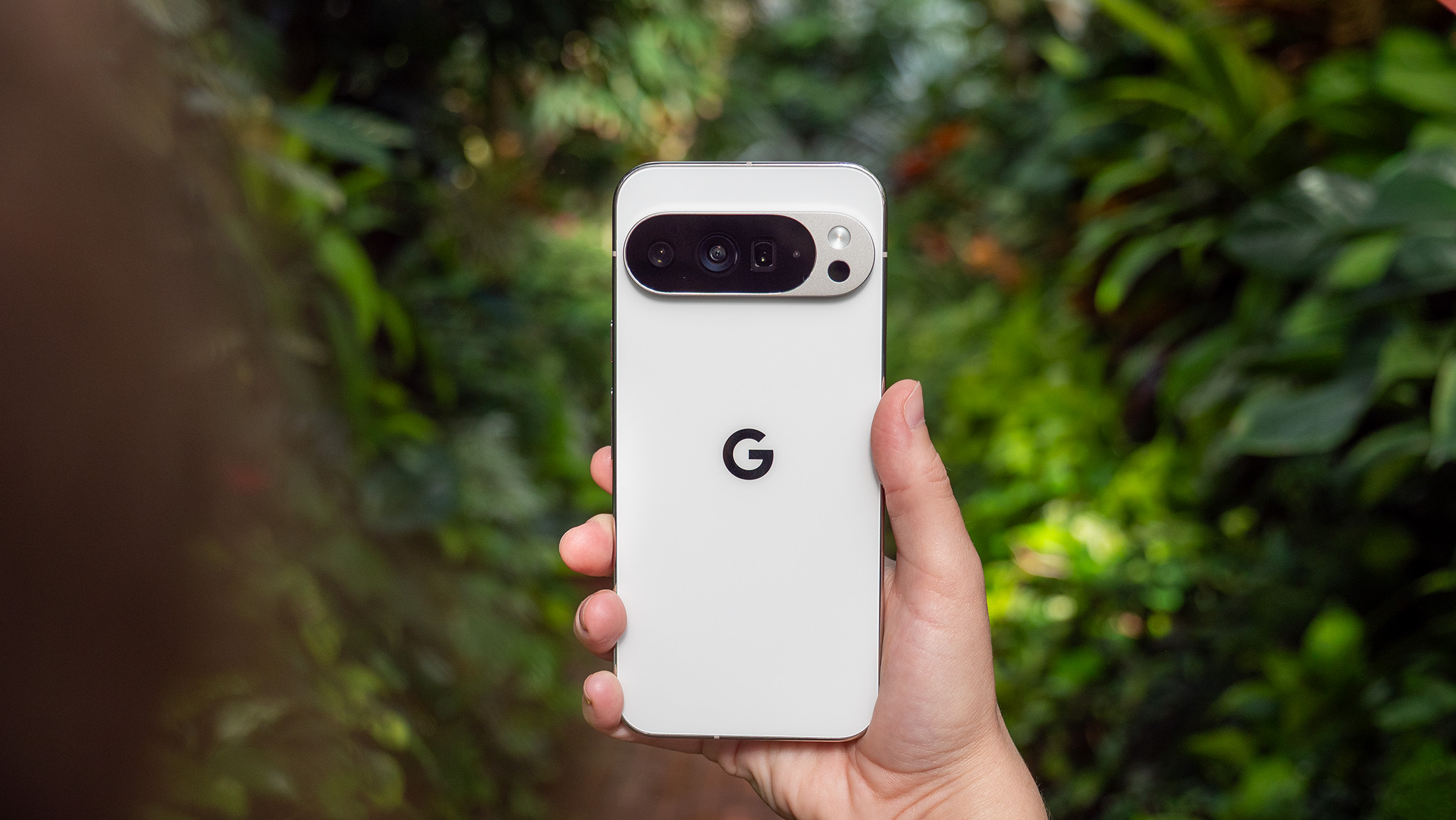 Holding a white Google Pixel 10 Pro XL with plants in the background