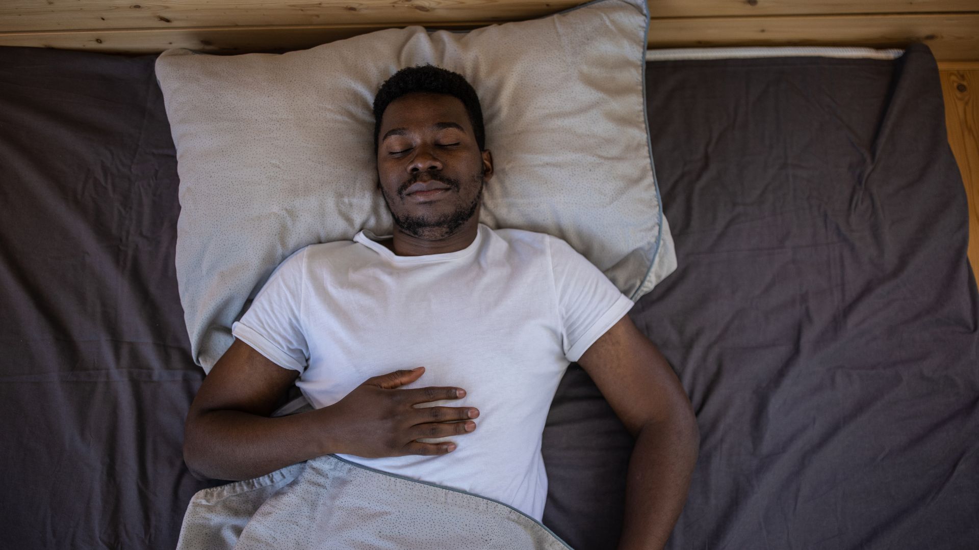 Ένας άντρας είναι ξαπλωμένος ανάσκελα στο κρεβάτι με τα μάτια κλειστά και το ένα χέρι ακουμπισμένο στο στήθος του.