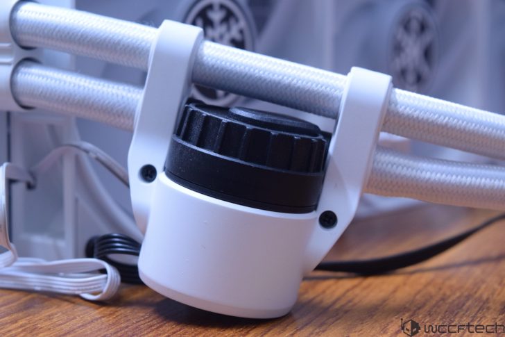 Κοντινό πλάνο ενός λευκού και μαύρου στοιχείου ψύξης με πλεγμένους σωλήνες, τοποθετημένο σε ξύλινη επιφάνεια, με το λογότυπο wccftech στη γωνία.