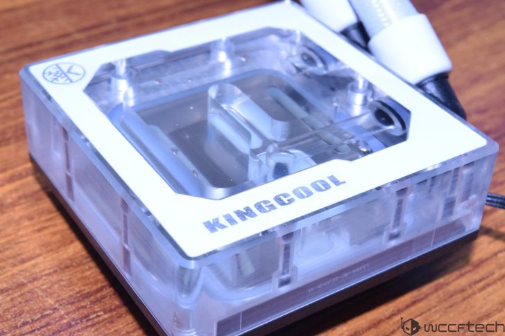 Σε μια ξύλινη επιφάνεια εμφανίζεται ένα μπλοκ νερού CPU επώνυμου Kingcool με διαφανές επάνω μέρος.