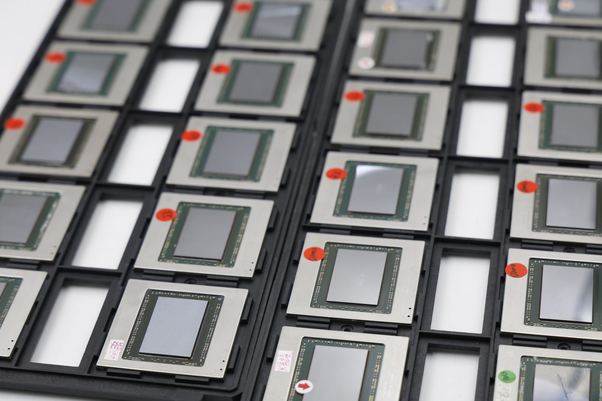 Ένας δίσκος χωρίς επώνυμο επεξεργαστές υπολογιστών με πράσινες πλακέτες κυκλωμάτων και πολλές κόκκινες ετικέτες, τοποθετημένοι σε μαύρες πλαστικές θήκες.