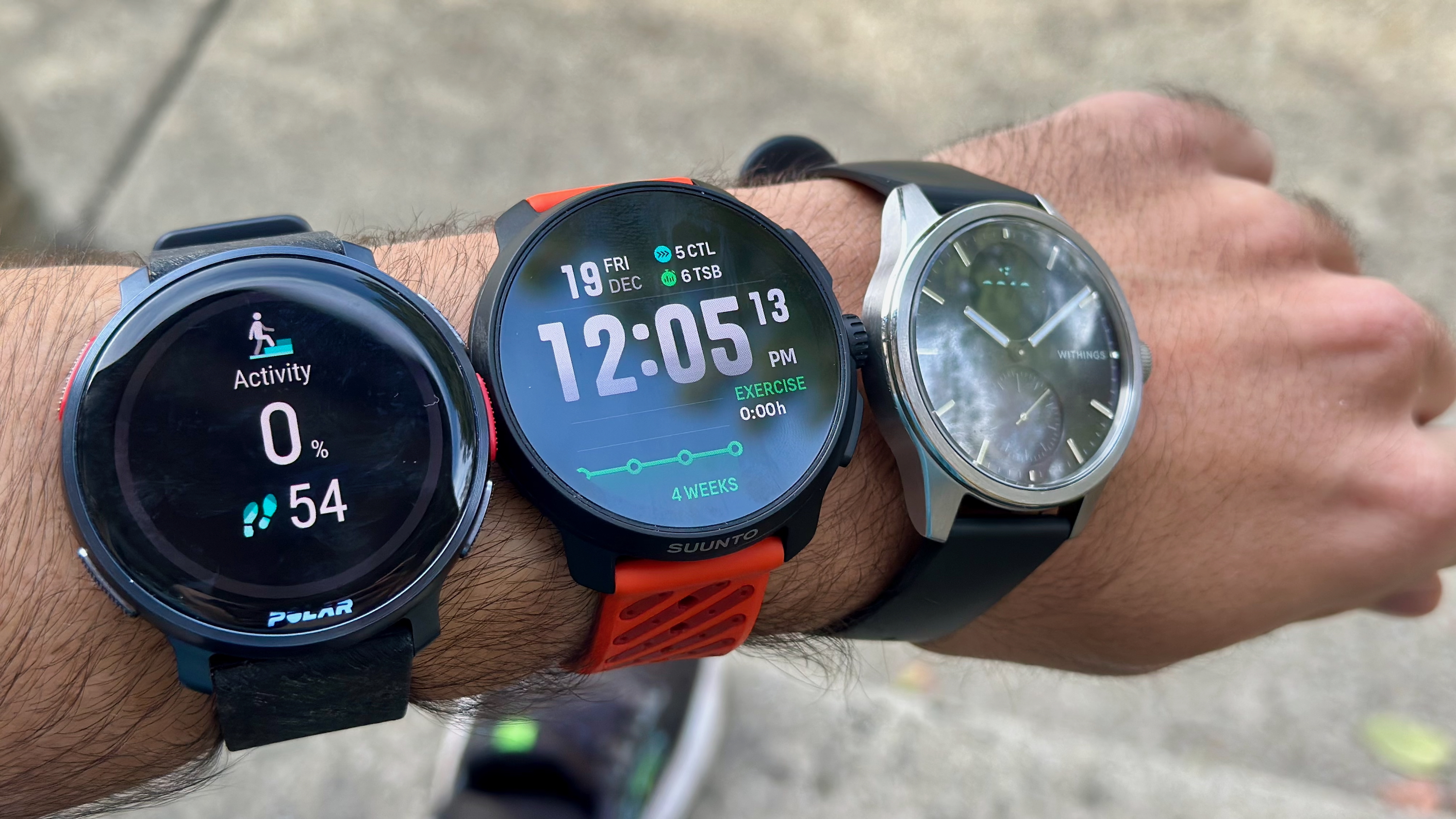 Μια φωτογραφία του Polar Vantage V3, του Suunto Race 2 και του Withings ScanWatch 2, όλα δεμένα σε έναν βραχίονα.