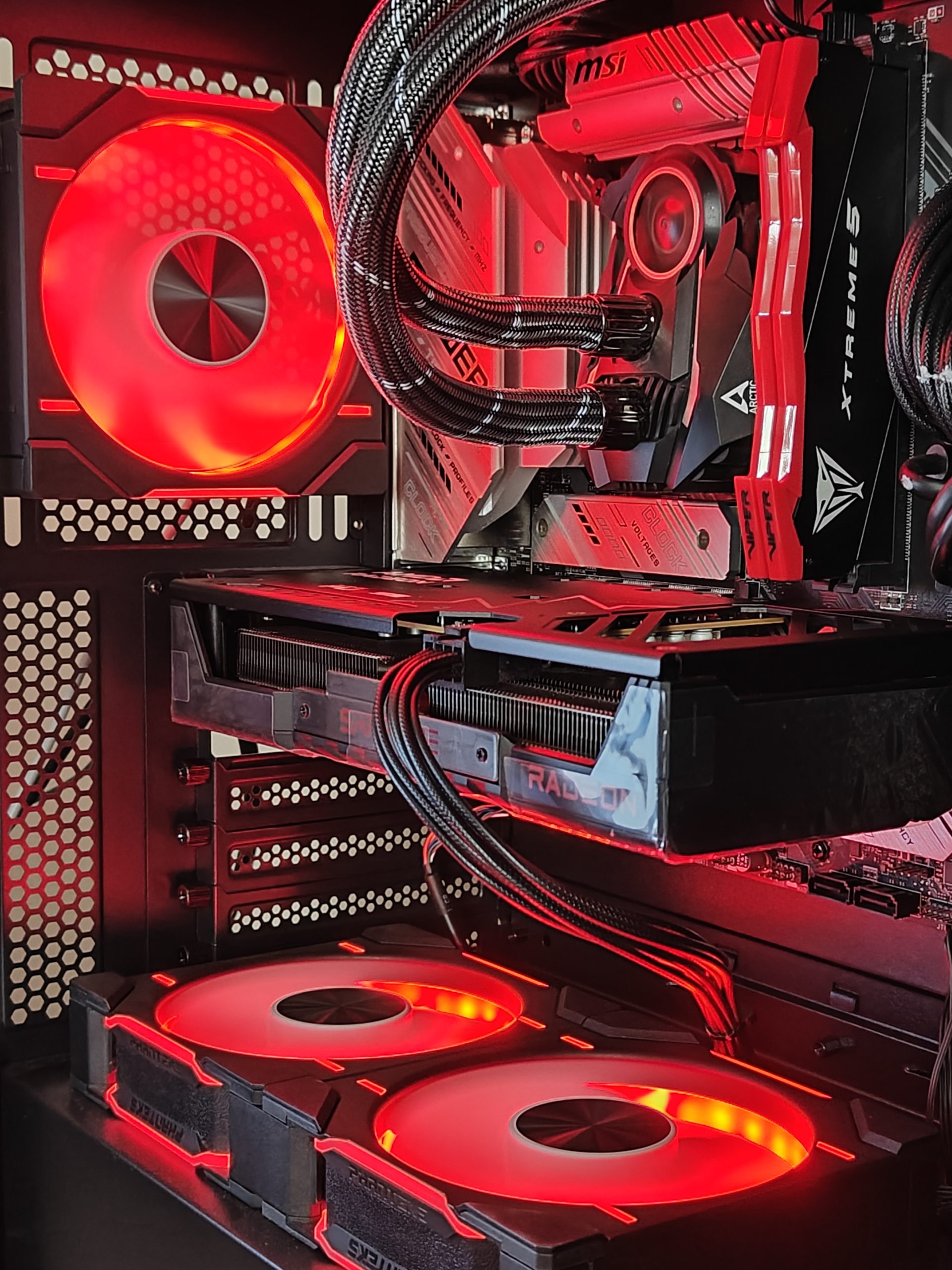 Ένα εσωτερικό υπολογιστή παιχνιδιών με κάρτα γραφικών MSI με την επωνυμία «XTREME 5», κάρτα γραφικών Radeon από κάτω και κόκκινους ανεμιστήρες LED.