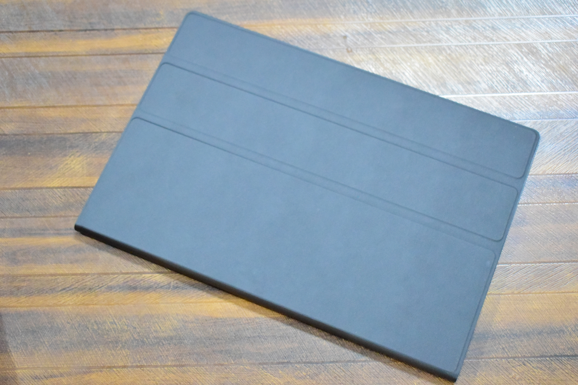 Φωτεινή φορητή οθόνη OLED 16 ιντσών 3K Μια κλειστή μαύρη θήκη tablet βρίσκεται σε μια ξύλινη επιφάνεια.