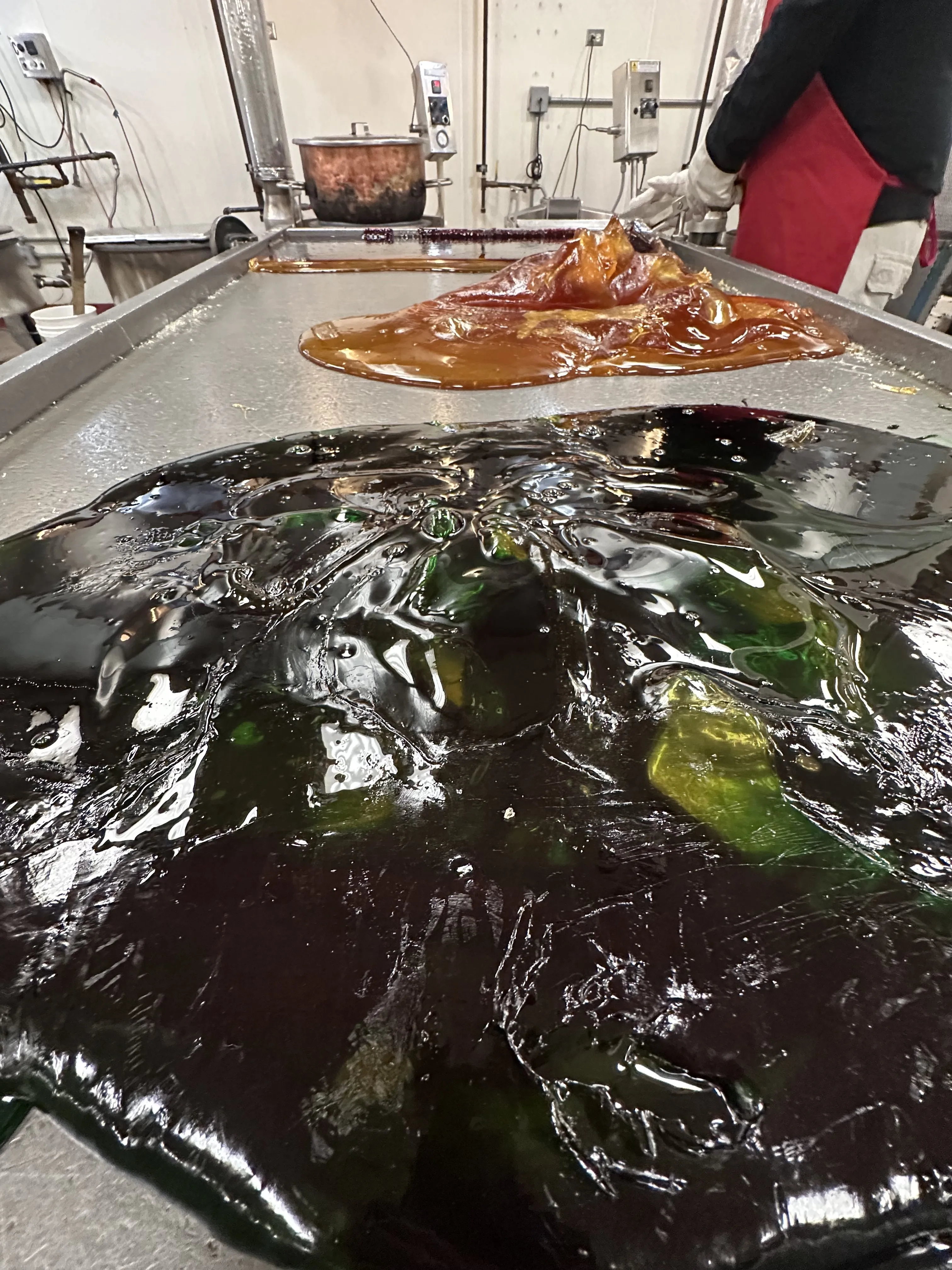 Η μαγεία της κατασκευής ζαχαροκάλαμων στο χέρι μια πορτοκαλί και πράσινη σταγόνα υγροποιημένης καραμέλας σε ένα τραπέζι από χάλυβα