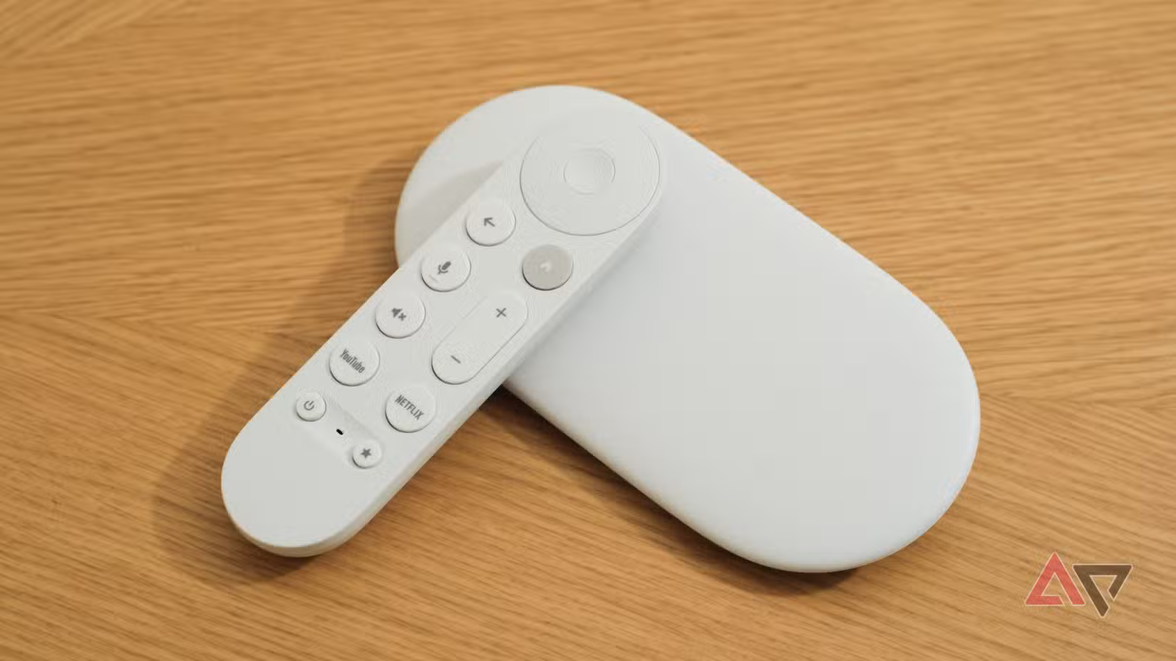 Το Google TV Streamer με το τηλεχειριστήριο ακουμπισμένο πάνω του σε ξύλινη επιφάνεια.