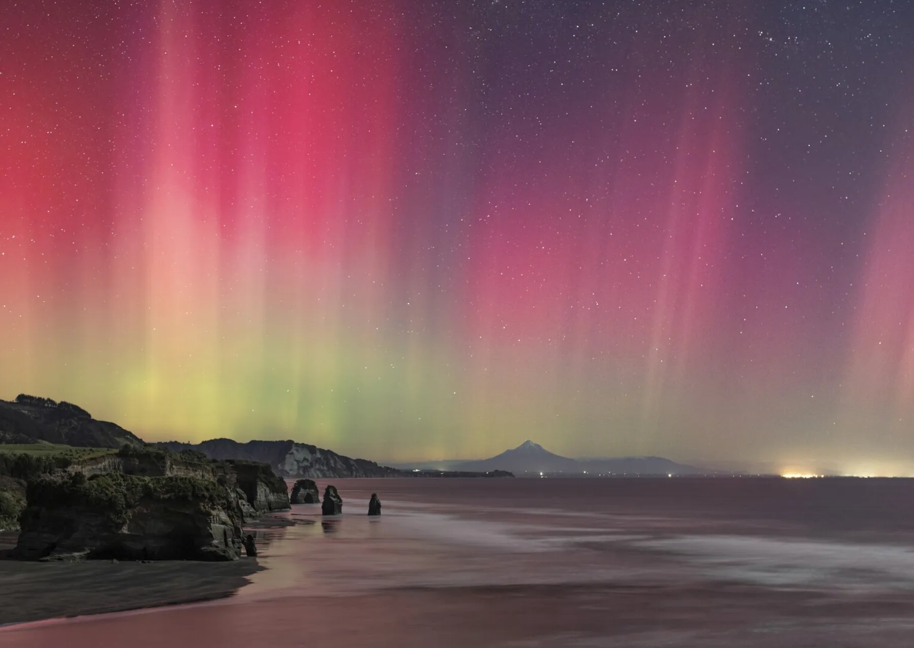 a pink and yellow aurora glows over a beach with large standing stones