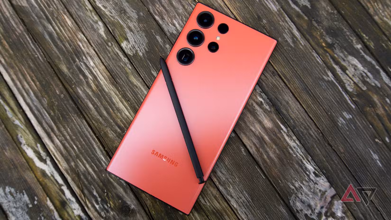 Μια φωτογραφία ενός κόκκινου Galaxy S23 Ultra με την όψη προς τα κάτω σε μια ξύλινη επιφάνεια με το S Pen να βρίσκεται στην κορυφή