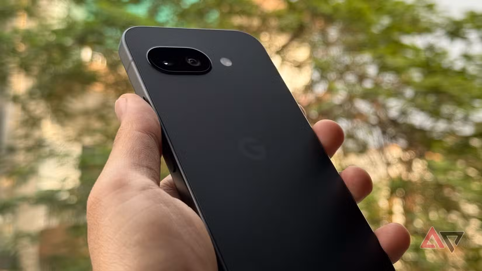 Γωνιακή λήψη του μαύρου Pixel 9a που κρατήθηκε σε εξωτερικούς χώρους, δείχνοντας το σχέδιο της πλάτης