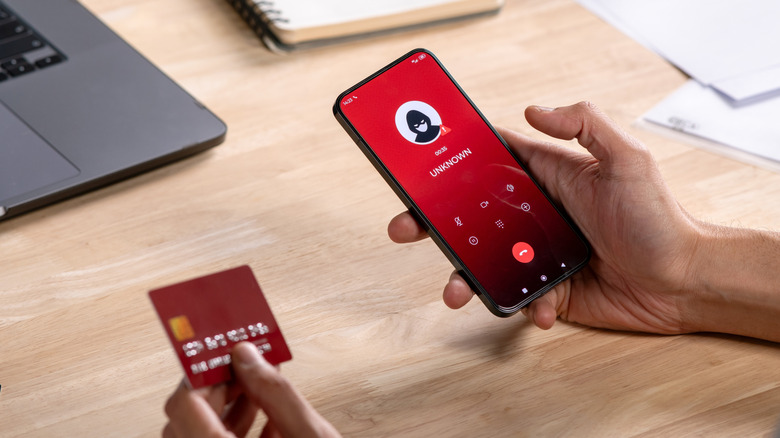 Ένα άτομο που κρατά μια πιστωτική κάρτα δίπλα σε ένα τηλέφωνο με έναν άγνωστο καλούντα