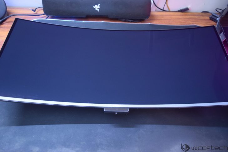 A curved MSI gaming monitor with a Razer soundbar placed behind it on a desk.