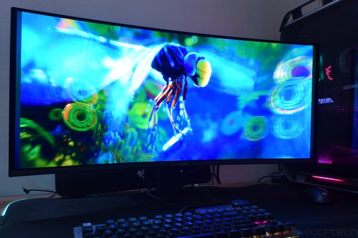 A Razer logo is visible on a monitor displaying a vibrant, colorful digital artwork of an insect, with an MSI keyboard below and an illuminated PC housing with visible 'GEFORCE' text nearby.