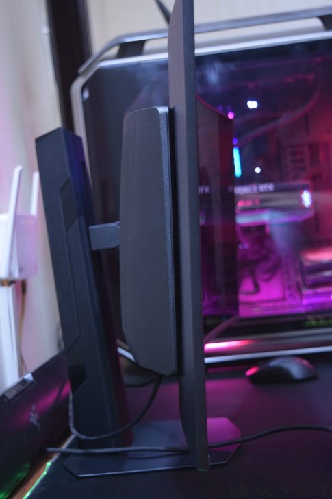 A side view of a computer monitor with a thin black bezel next to a gaming PC featuring a visible NVIDIA RTX graphics card inside a case with purple lighting.