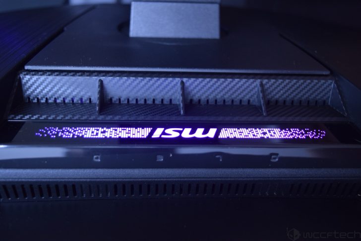 Close-up of an MSI gaming monitor with carbon fiber accents and a glowing MSI logo.