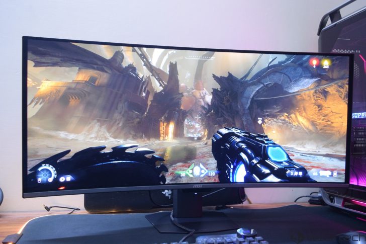 A curved MSI monitor displays a scene from the game DOOM Eternal, with visible health and armor indicators.