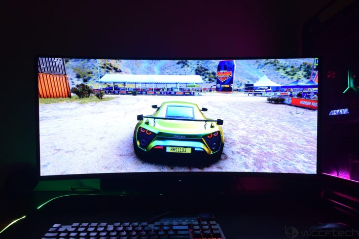 A racing scene from the game 'Horizon' is displayed on a curved monitor, showing a green car with the license plate 'HMS1193,' while a 'SUPRIM' branded gaming PC glows in the background.