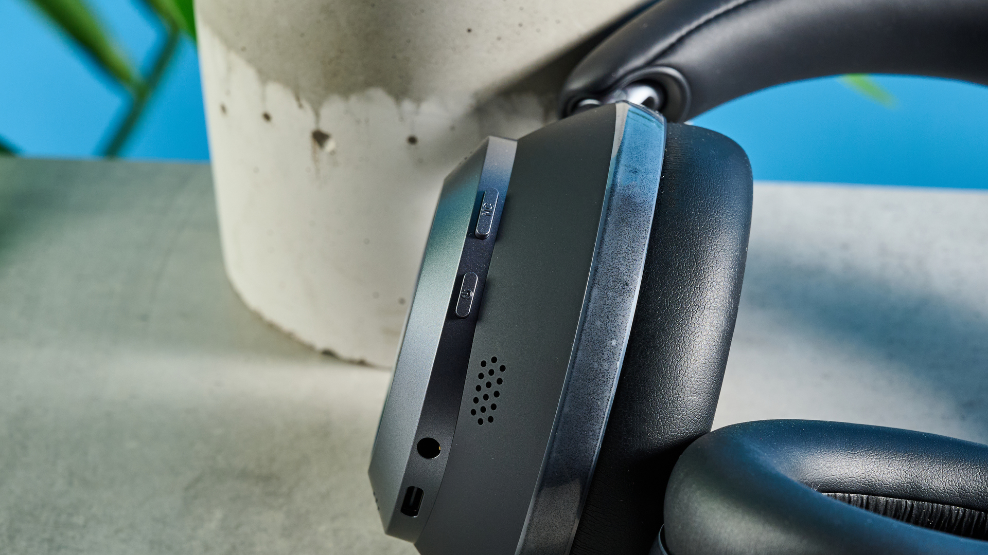 μια φωτογραφία ενός ζευγαριού μαύρων ακουστικών πάνω από το αυτί με μαλακά κύπελλα και ένα μαλακό κεφαλόδεσμο, φωτογραφημένη μπροστά σε μπλε φόντο