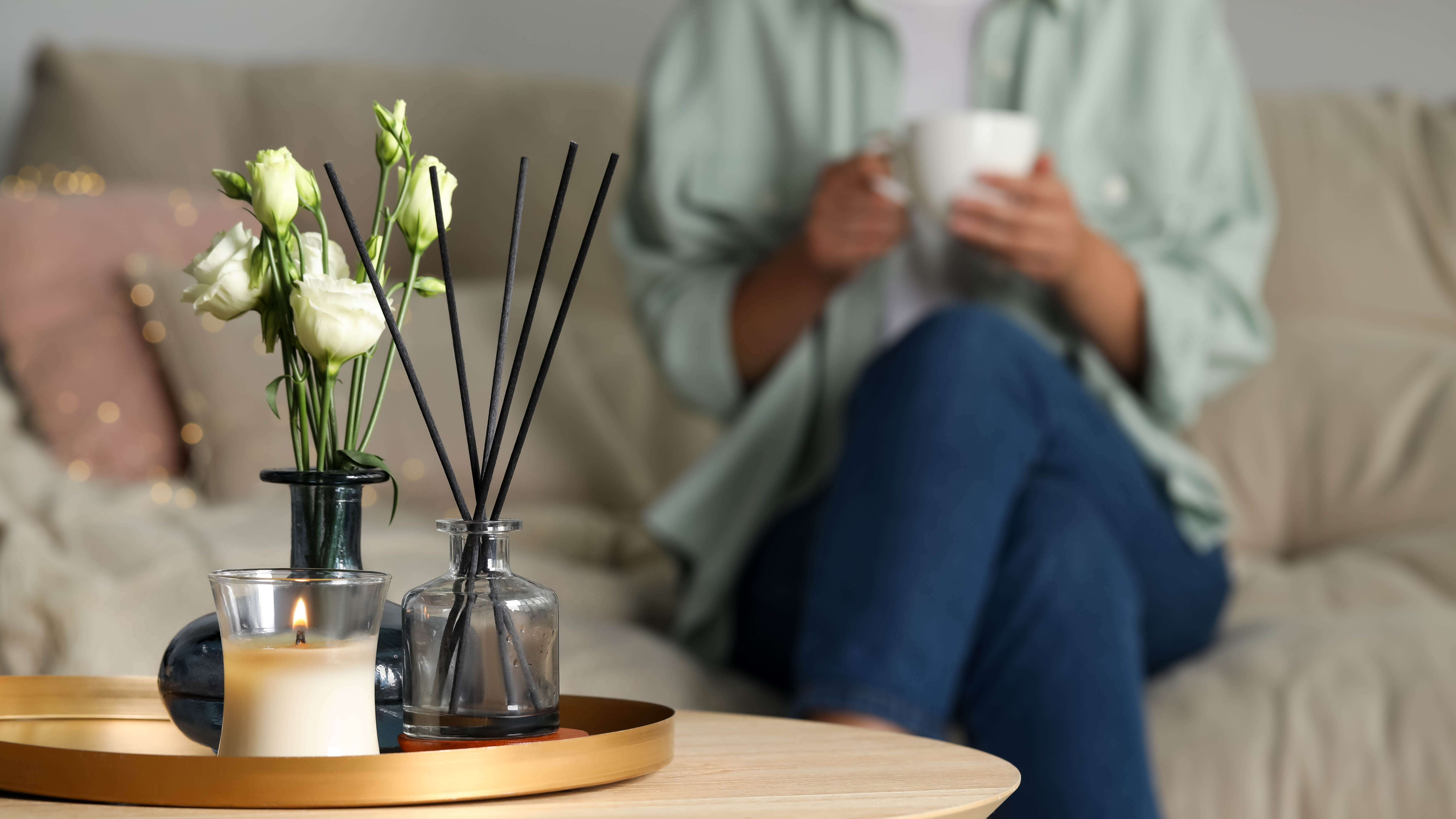 Κερί και διαχύτης στο τραπεζάκι του καφέ με γυναίκες που κάθονται στον καναπέ κρατώντας μια λευκή κούπα