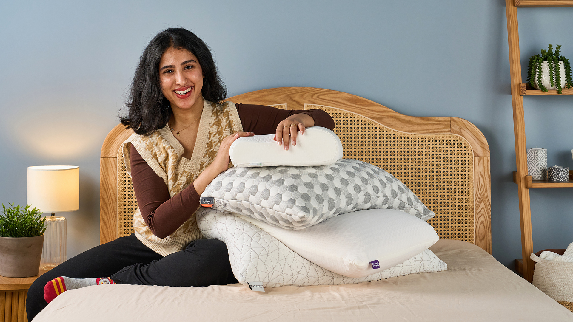 Γυναίκα που κρατά μια στοίβα από μαξιλάρια στο κρεβάτι με ένα κομοδίνο και ξενύχτι δίπλα του