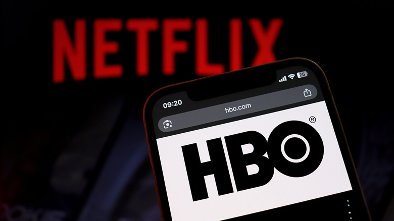 Το λογότυπο του HBO σε ένα smartphone και το λογότυπο του Netflix θαμπωμένο στο φόντο.