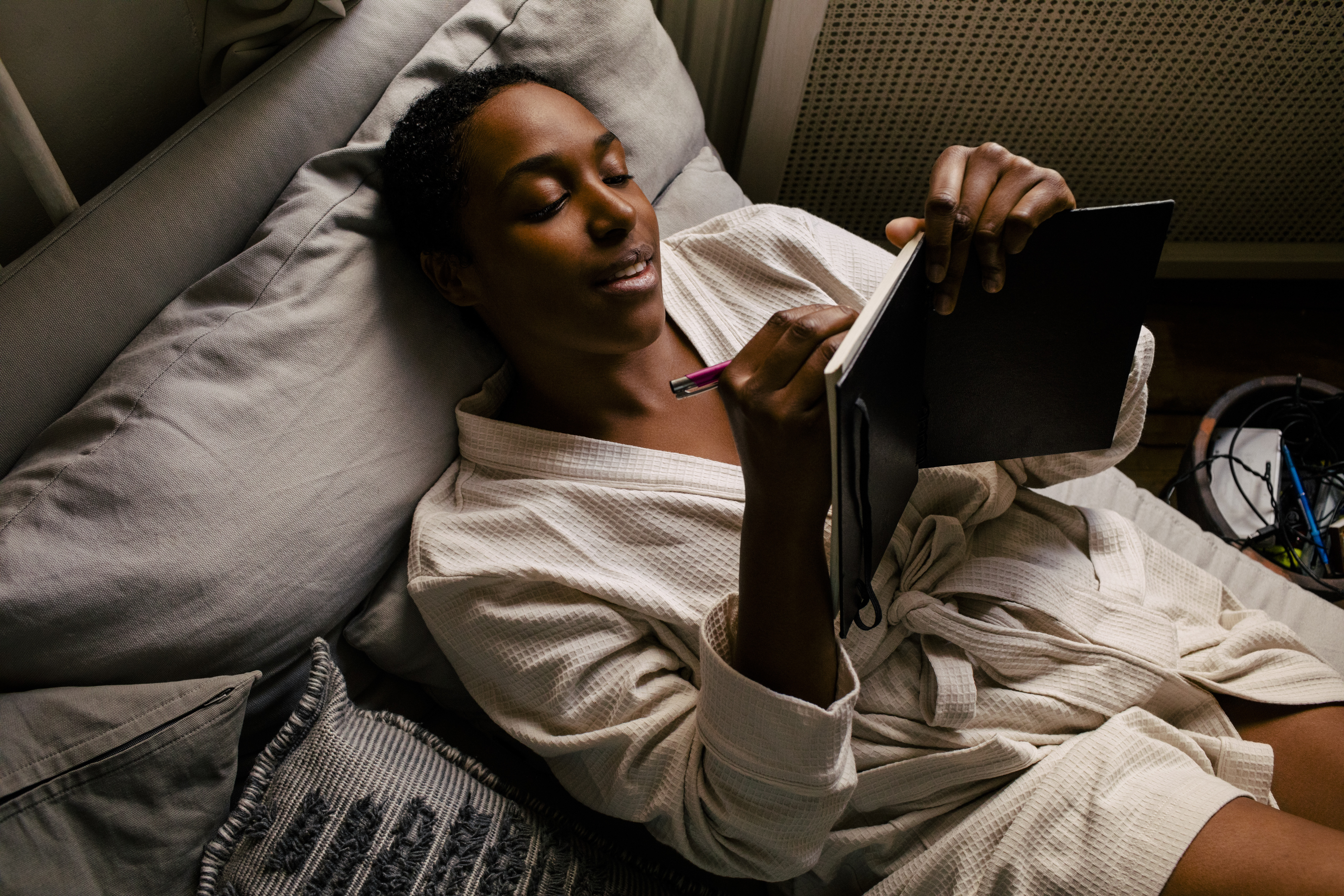 Μια γυναίκα ξαπλώνει στο κρεβάτι φορώντας μια ρόμπα καθώς γράφει σε ένα ημερολόγιο.