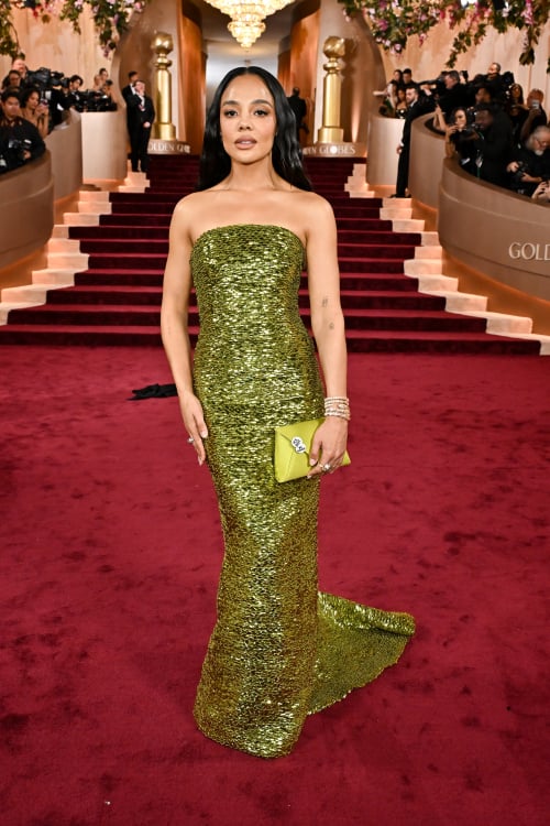 Η Tessa Thompson κρατά μια πράσινη τσάντα clutch με δύο καρφίτσες #BeGood, διαβάζοντας 