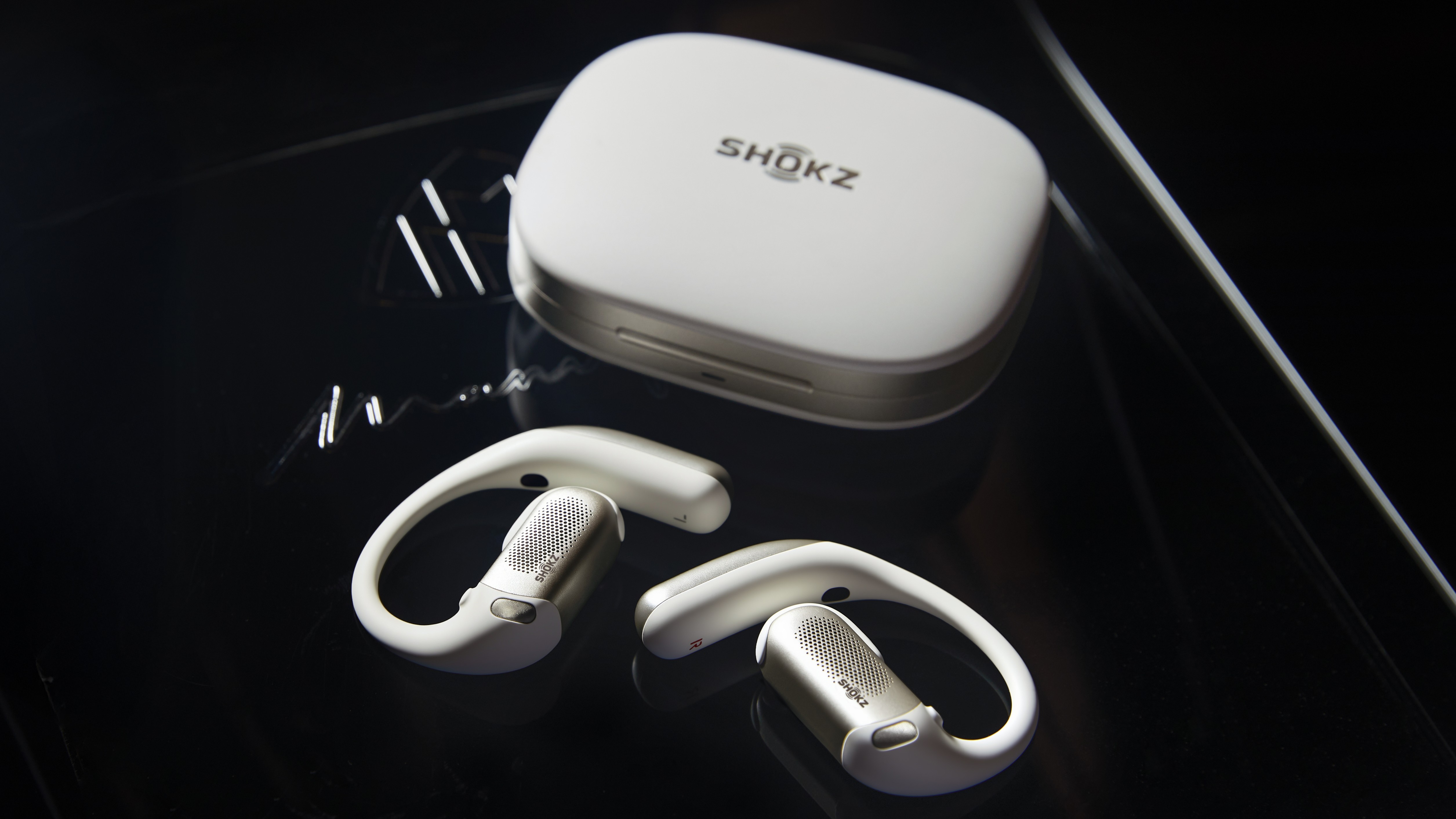 Πατήστε φωτογραφία των ακουστικών Shokz OpenFit Pro και της θήκης φόρτισης που βρίσκονται σε μαύρη επιφάνεια.