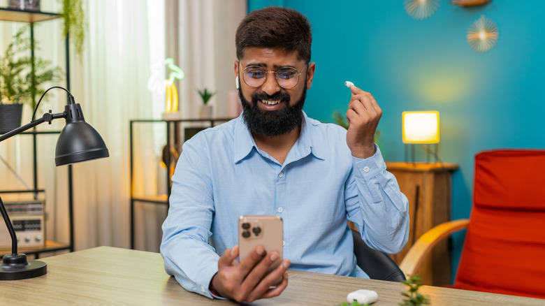 ένας απογοητευμένος άνδρας βγάζει ένα ακουστικό και κοιτάζει το τηλέφωνό του