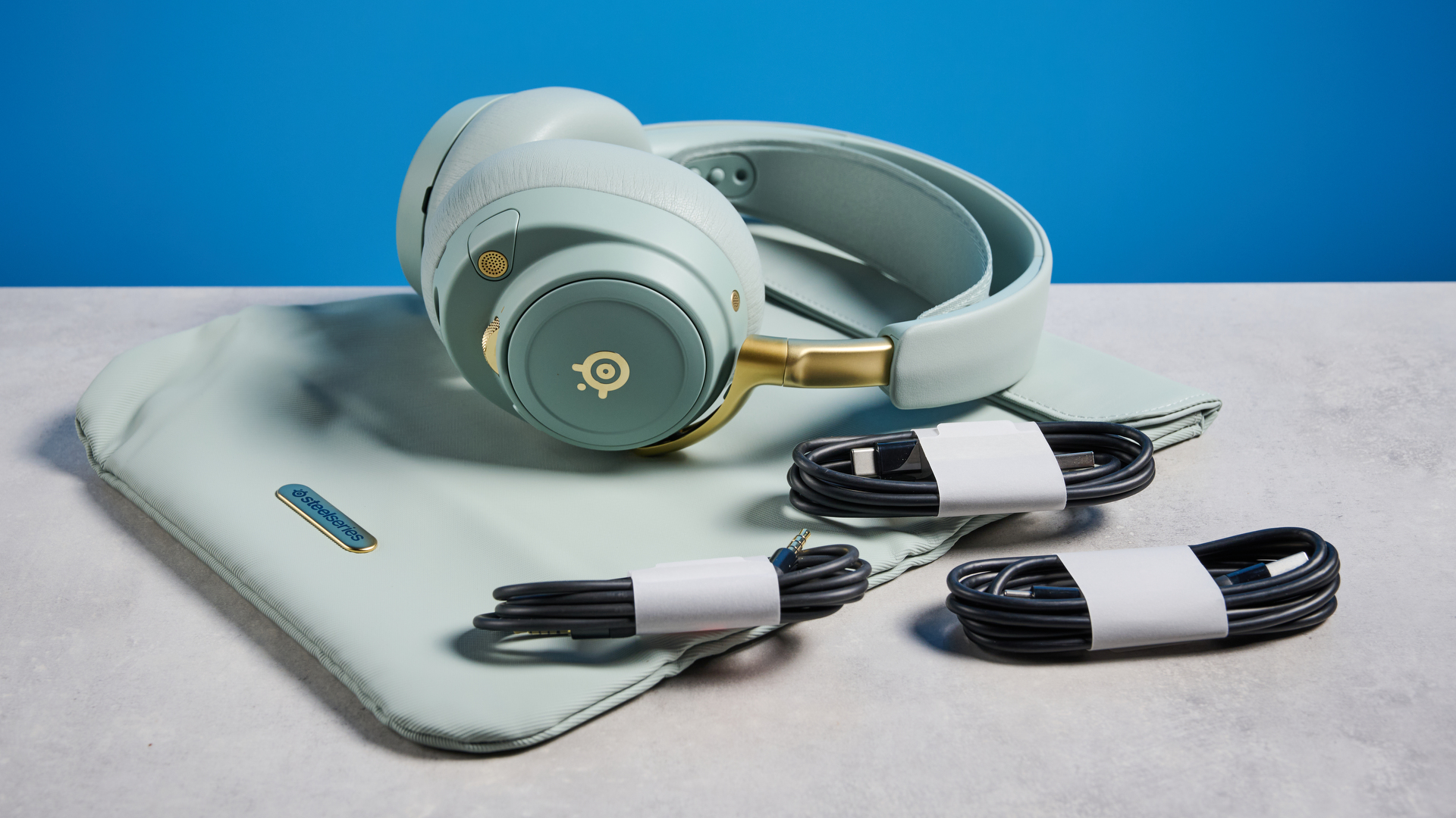 The SteelSeries Arctis Nova Elite with a carry pouch and its cables on a stone surface