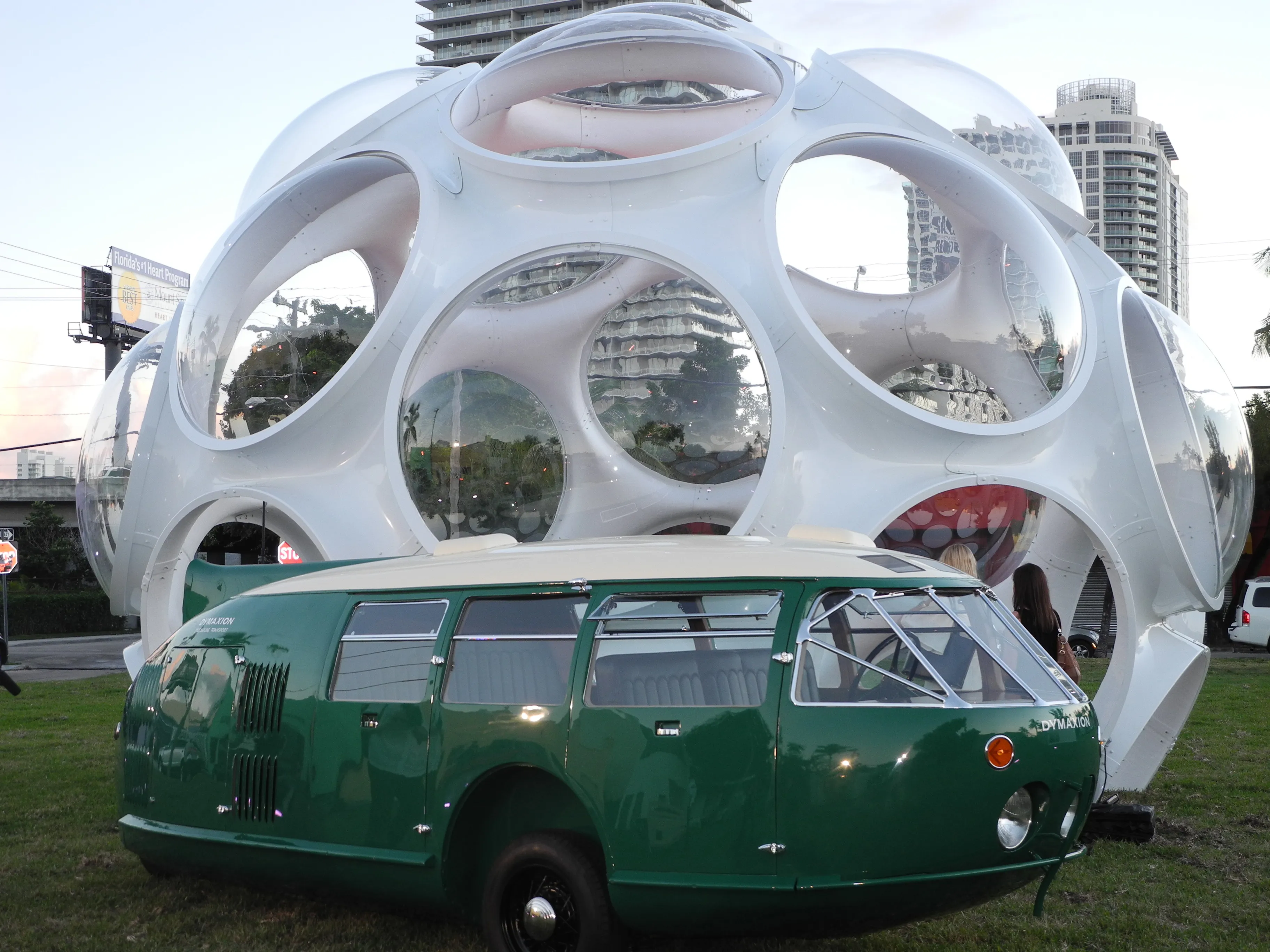A green teardrop-shaped vintage car is parked in front of a futuristic-looking sphere.