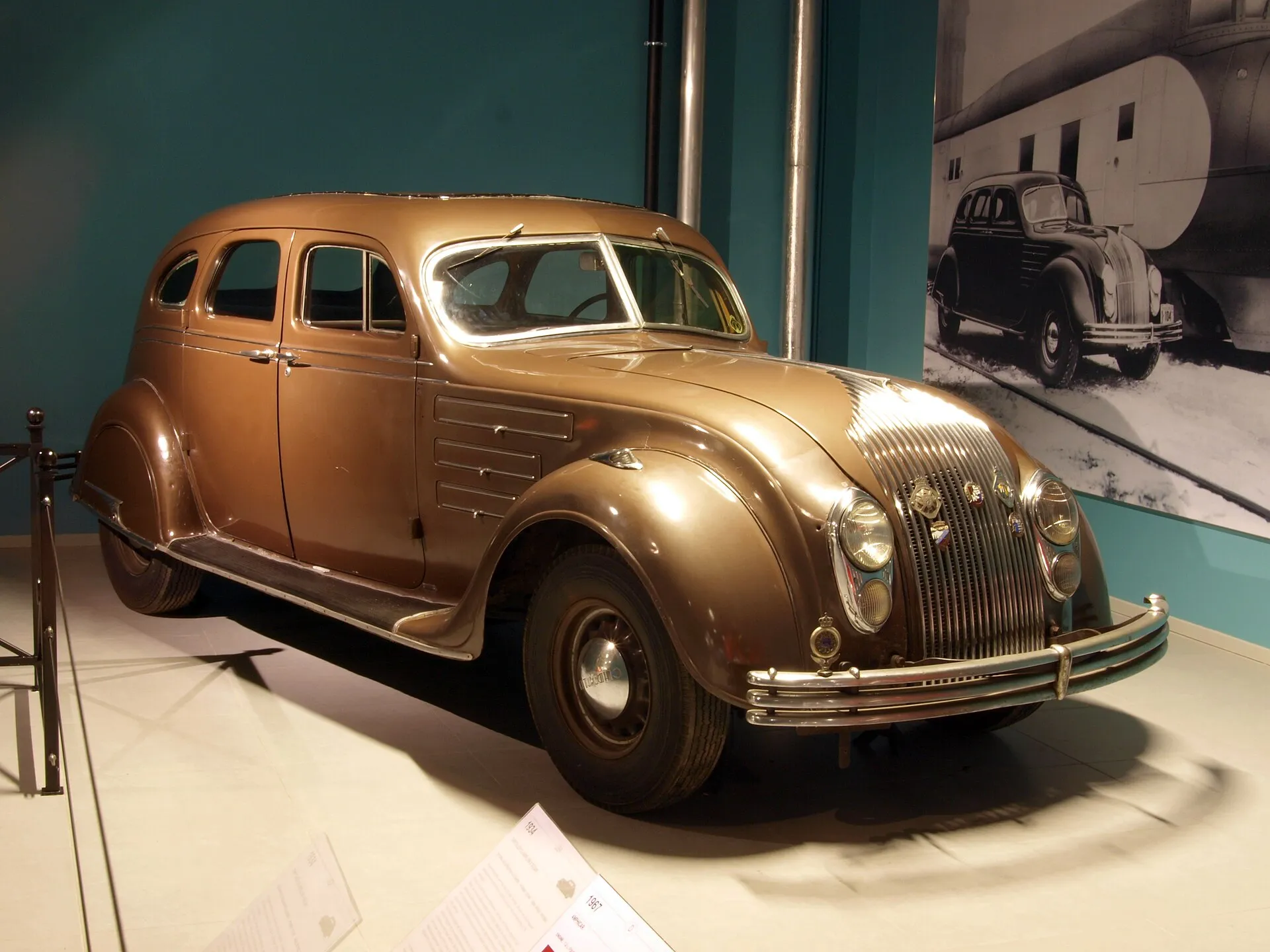 A orange/gold vintage 1934 Chrysler Airflow car with an aerodynamic hood in a showroom.