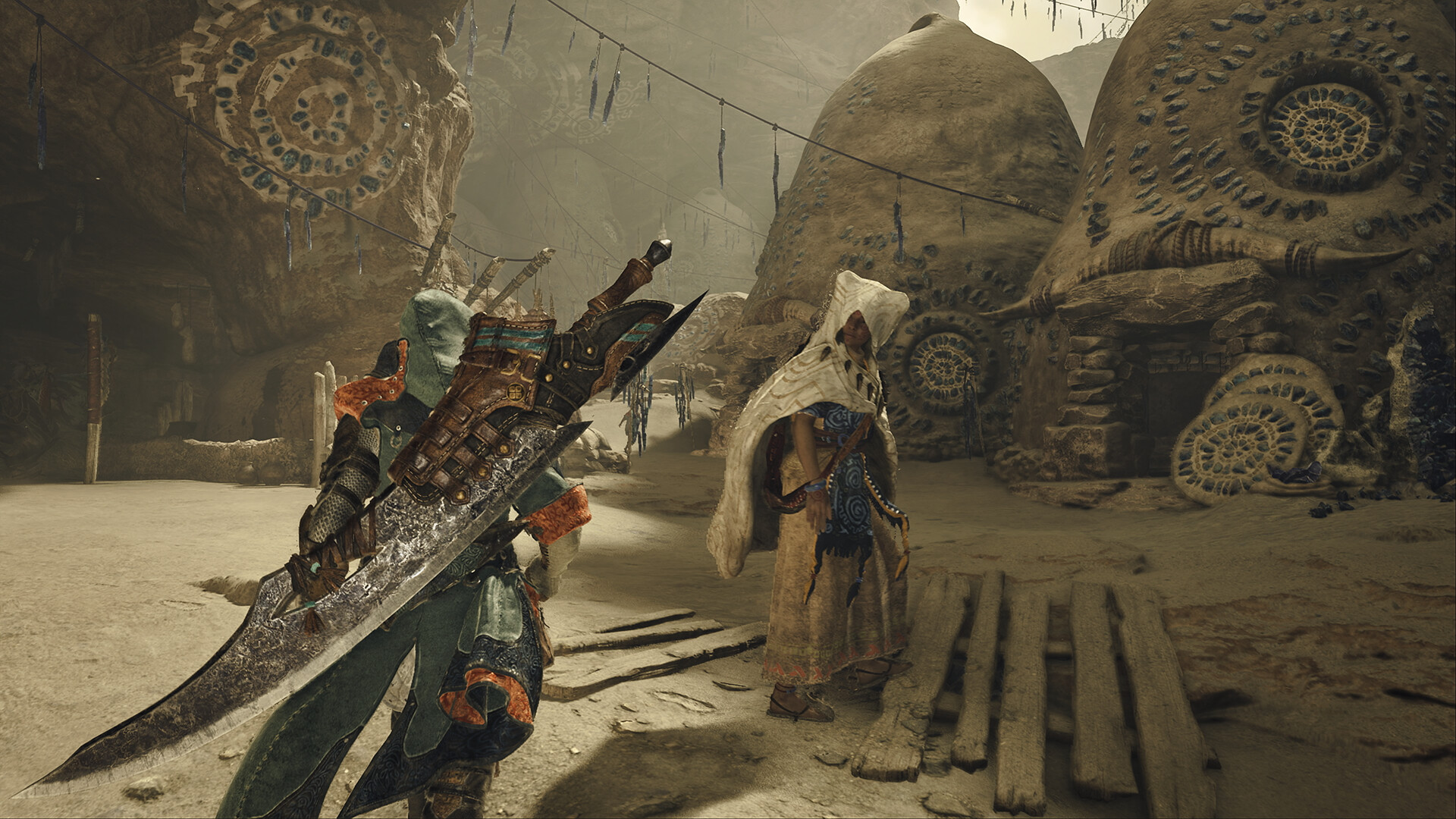 A character in a hooded outfit with a large sword explores a desert village with spiral patterns on the walls in the game Atlas Fallen.