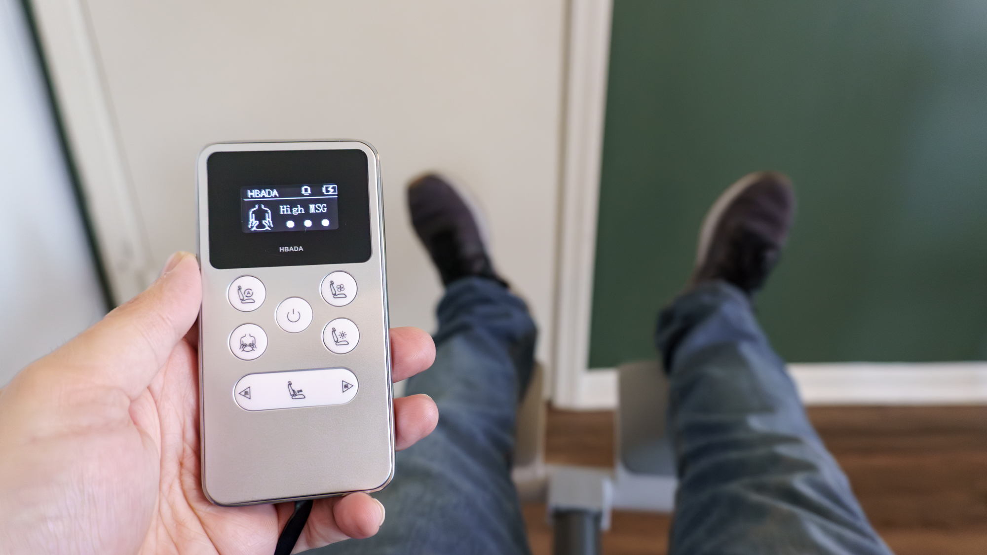 A person holding the remote for the Hbada X7 office chair while reclining in it with their feet up