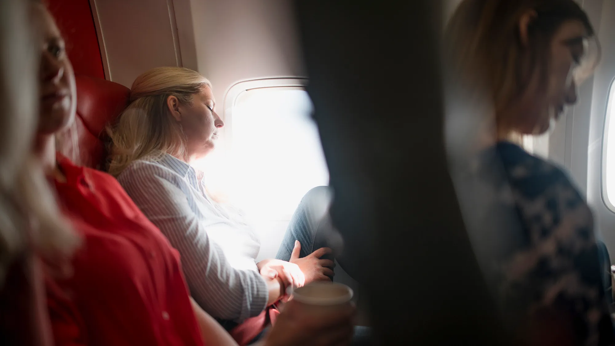 Η ώριμη γυναίκα κοιμάται σε ένα αεροπλάνο στην οικονομική θέση. Είναι ξανθιά με μπλε και άσπρο ριγέ κουμπί κάτω.