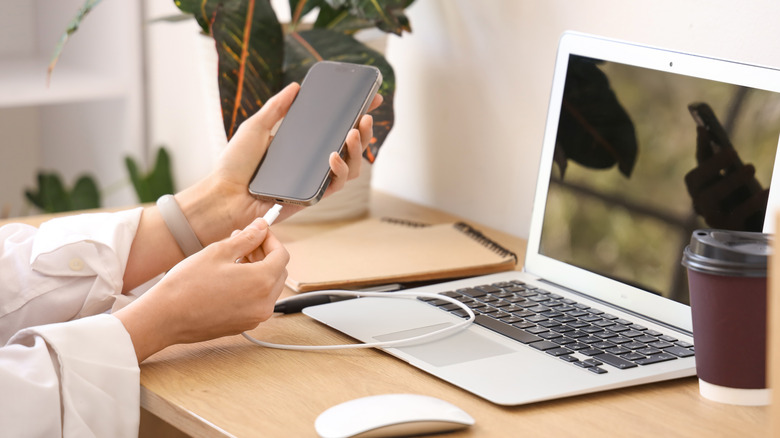 Κάποιος σε μια ρύθμιση γραφείου που συνδέει το smartphone του με έναν φορητό υπολογιστή κοντά