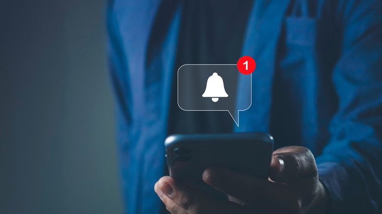 Ένα χέρι που κρατά ένα τηλέφωνο, με μια εννοιολογική απόδοση μιας ειδοποίησης εφαρμογής σε μια φυσαλίδα σκέψης πάνω από το τηλέφωνο