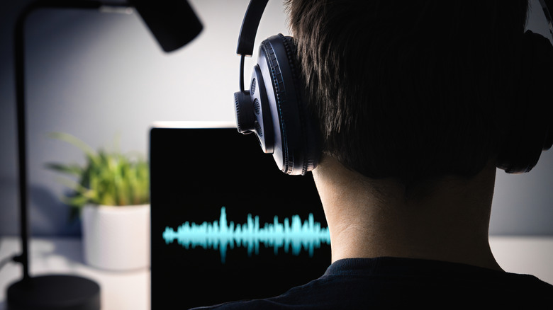 Ένα άτομο που ακούει ακουστικά κοιτάζοντας ένα γραφικό ηχητικών κυμάτων σε μια οθόνη υπολογιστή