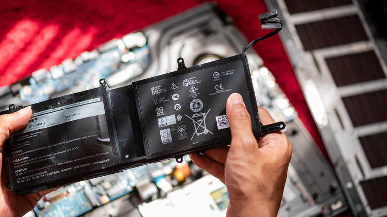 Ένα άτομο που κρατά μια διογκωμένη μπαταρία φορητού υπολογιστή πάνω από ένα αποσυναρμολογημένο φορητό υπολογιστή
