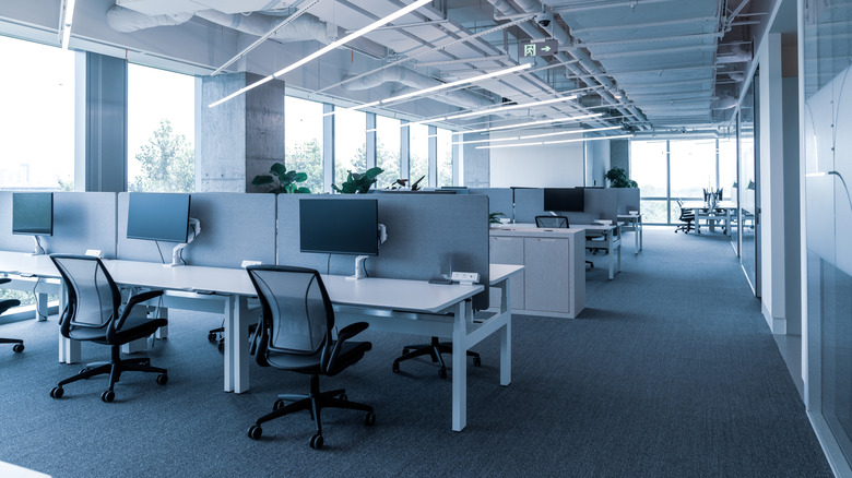 Σύγχρονη ανοιχτή κάτοψη γραφείου με ορατές πολλές οθόνες υπολογιστών και γραφεία.