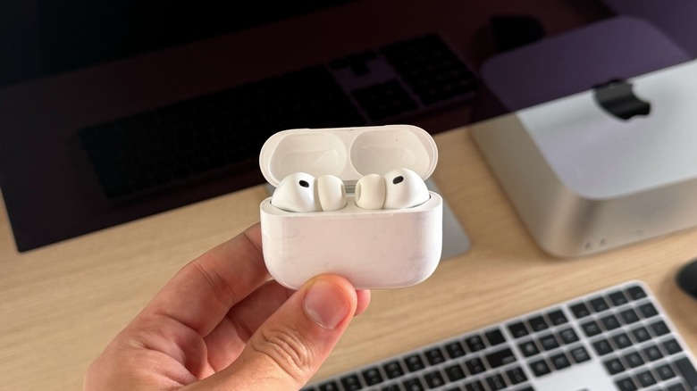 Τα ακουστικά AirPods Pro 3 της Apple μέσα στη θήκη φόρτισης. Το Mac Studio και το Studio Display βρίσκονται πίσω από τα ακουστικά.