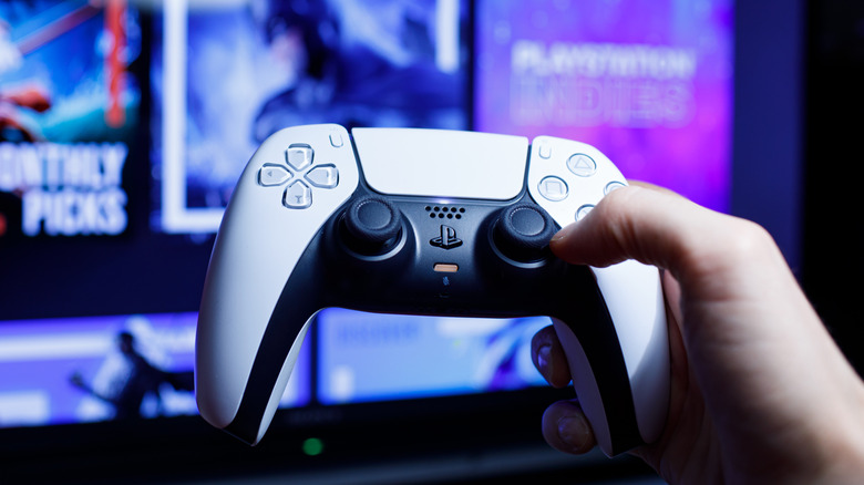 Χέρι που κρατά το χειριστήριο PlayStation 5 DualSense μπροστά από την οθόνη της τηλεόρασης