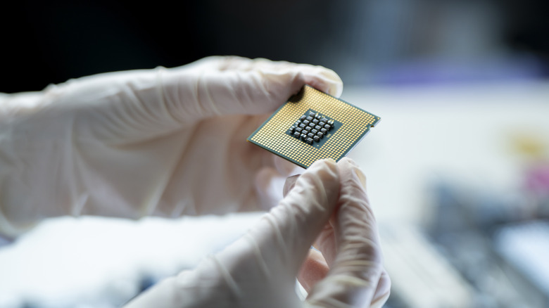 Κάποιος φοράει γάντια κρατώντας ένα τσιπ υπολογιστή με το κάτω μέρος ανοιχτό.