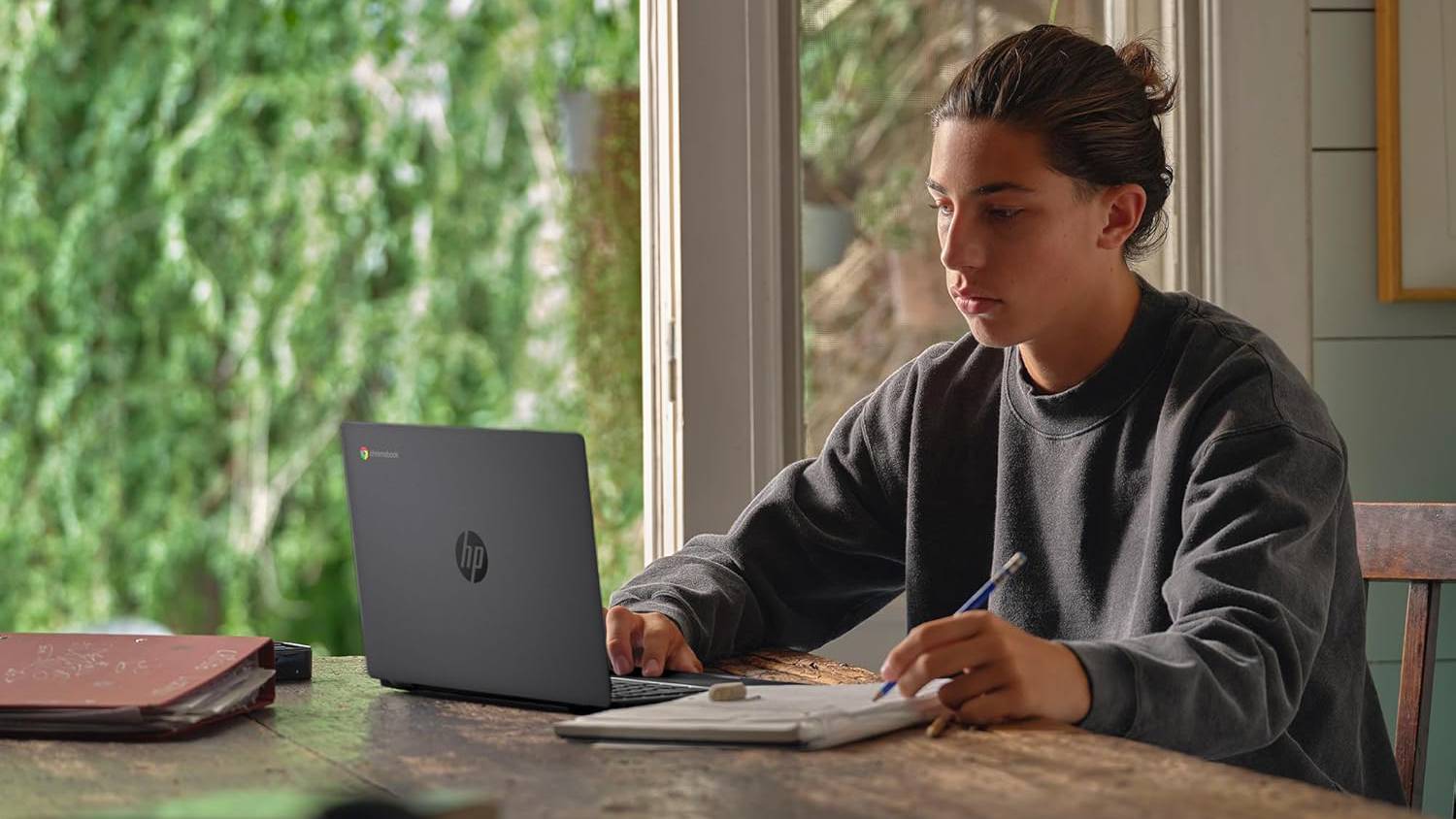 Άτομο που χρησιμοποιεί HP Chromebook 14 στο τραπέζι της κουζίνας ενώ γράφει στο σημειωματάριο